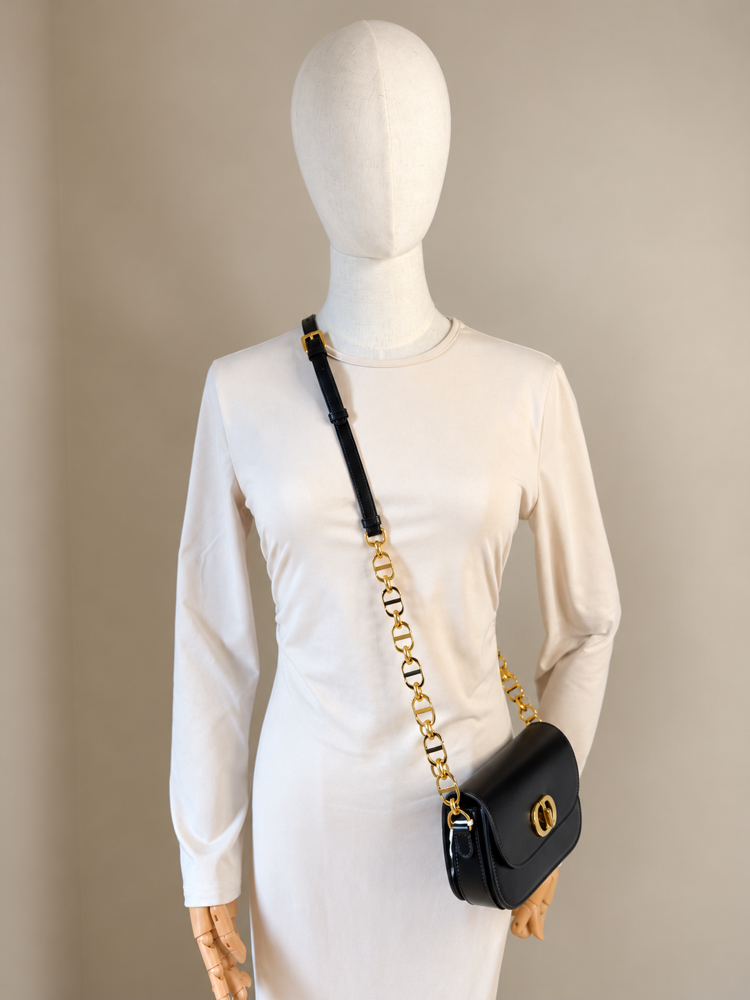 A black leather Dior shoulder bag with a gold-tone chain strap and cd logo clasp, displayed on a white long-sleeve mannequin dress against a neutral beige background.