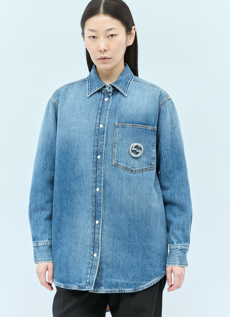 A model wearing a light blue Gucci denim button-up jacket with a chest pocket featuring a Gucci logo brooch 